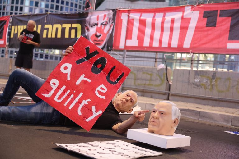 A demonstrator wearing a mask representing Israel's Prime Minister Benjamin Netanyahu lifts a placard during a recent anti-government protest by Israeli activists in Tel Aviv. (AFP)